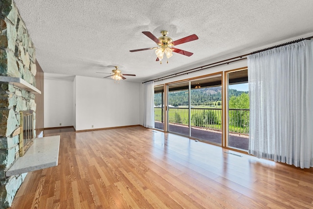 252 Davaz-Carlton Rd, Newport, WA 99156 - unfurnished living room with a ceiling fan, light wood-style flooring, a textured ceiling, baseboards, and a stone fireplace