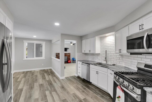 8428 N Susan Ct, Spokane, WA 99208 - kitchen with appliances with stainless steel finishes, a ceiling fan, a fireplace, a sink, and light stone countertops