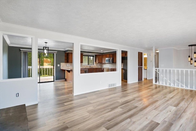 6106 W Kittitas Ct, Spokane, WA 99208 - unfurnished living room featuring a textured ceiling, light wood-style flooring, ornamental molding, a chandelier, and a sink