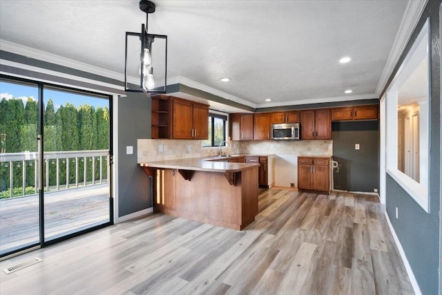 6106 W Kittitas Ct, Spokane, WA 99208 - kitchen featuring stainless steel microwave, a peninsula, tasteful backsplash, light wood-type flooring, and ornamental molding