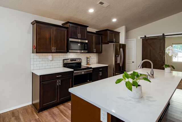 704 E Canterbury Ln, Colbert, WA 99005 - kitchen featuring stainless steel appliances, light wood-style floors, light countertops, decorative backsplash, and a kitchen island with sink