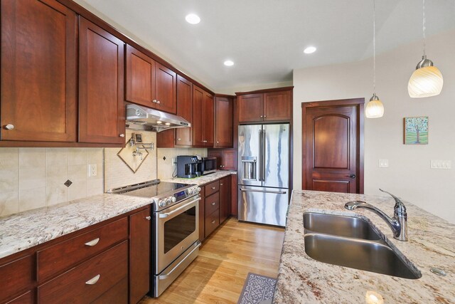 1002 N High Desert Dr, Deer Park, WA 99006 - kitchen with under cabinet range hood, stainless steel appliances, a sink, hanging light fixtures, and light stone counters