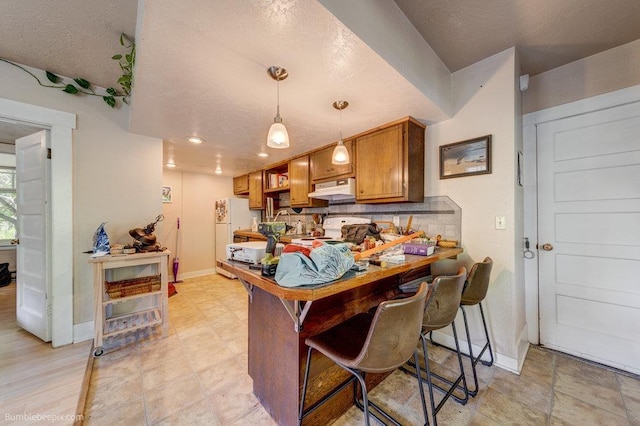 1611 W 9th Ave, Spokane, WA 99223 - kitchen featuring under cabinet range hood, stove, brown cabinetry, freestanding refrigerator, and baseboards