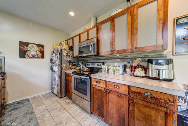 1611 W 9th Ave, Spokane, WA 99223 - kitchen with appliances with stainless steel finishes, light countertops, brown cabinetry, light tile patterned flooring, and baseboards