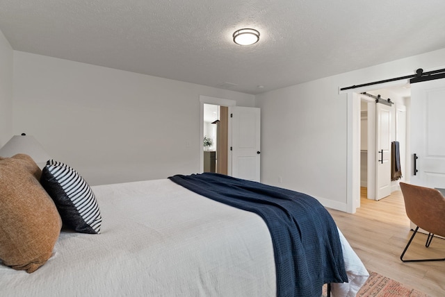 14101 E Sanson Ave, Spokane Valley, WA 99216 - bedroom with a barn door, light wood-style floors, a spacious closet, baseboards, and a textured ceiling