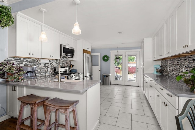 1306 W Euclid Ave, Spokane, WA 99205 - kitchen featuring appliances with stainless steel finishes, a peninsula, tasteful backsplash, white cabinetry, and a kitchen bar