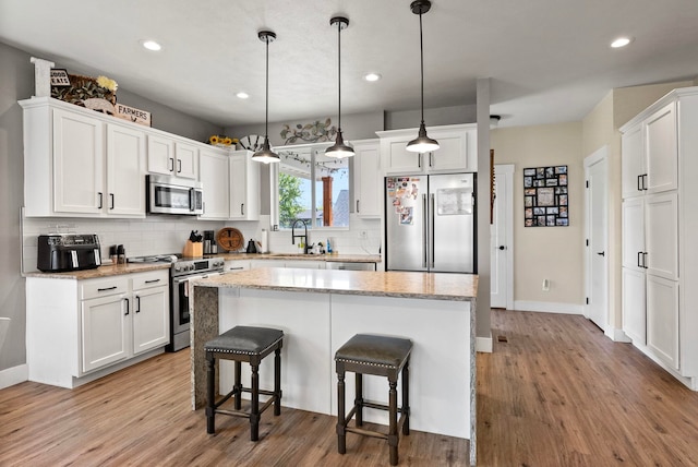 1812 E Columbia Ave, Spokane, WA 99208 - kitchen with appliances with stainless steel finishes, white cabinets, light wood finished floors, decorative backsplash, and a breakfast bar area
