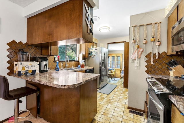 4405 E 46th Ave, Spokane, WA 99223 - kitchen with a sink, appliances with stainless steel finishes, a peninsula, backsplash, and brown cabinets