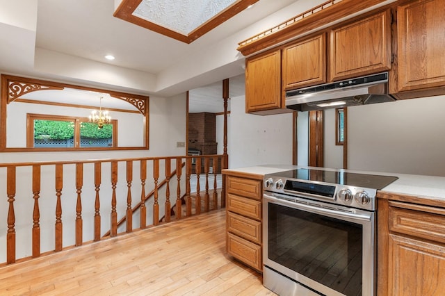 1621 E 65th Ave, Spokane, WA 99223 - kitchen with stainless steel electric stove, under cabinet range hood, brown cabinets, light wood-style flooring, and a chandelier