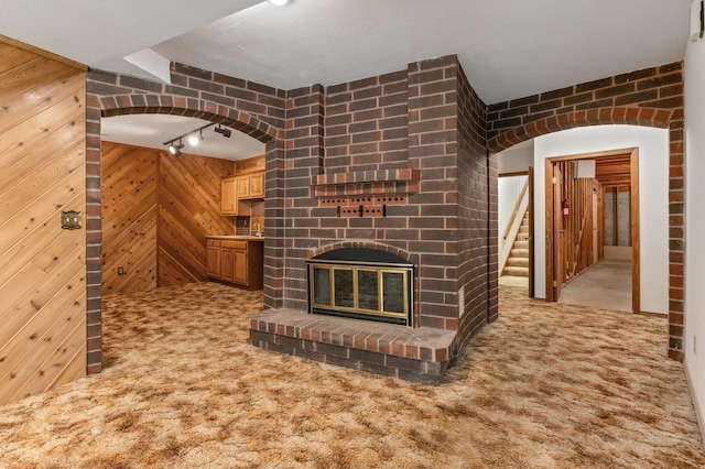 1621 E 65th Ave, Spokane, WA 99223 - unfurnished living room featuring carpet flooring, rail lighting, a brick fireplace, wood walls, and arched walkways