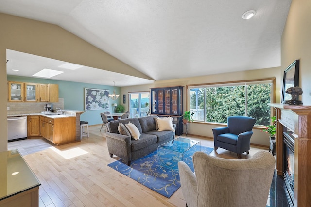 7802 E Timber Ridge Ln, Spokane Valley, WA 99212 - living room with lofted ceiling, a skylight, light wood-style floors, a glass covered fireplace, and a chandelier