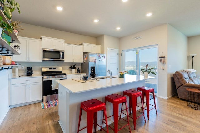 5414 E Bridgeport Ct, Spokane, WA 99217 - kitchen featuring appliances with stainless steel finishes, a kitchen island with sink, light wood-style flooring, white cabinets, and a breakfast bar area