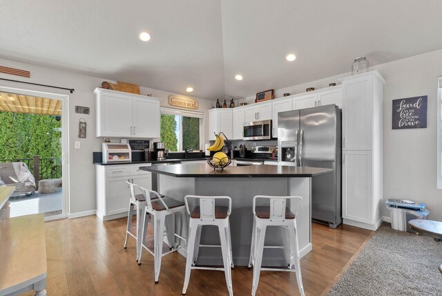 9805 N Jesse Ct, Spokane, WA 99208 - kitchen featuring appliances with stainless steel finishes, white cabinetry, light wood finished floors, a center island, and a breakfast bar area