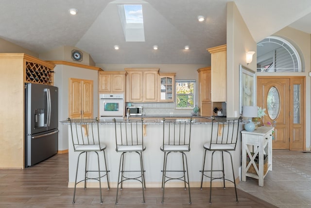 5506 S Southview Ln, Spokane, WA 99223 - kitchen featuring appliances with stainless steel finishes, a peninsula, vaulted ceiling, light stone counters, and tasteful backsplash