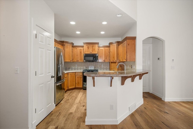 404 W Trail Ridge Ct, Spokane, WA 99224 - kitchen featuring stainless steel appliances, a peninsula, a kitchen breakfast bar, light wood finished floors, and decorative backsplash