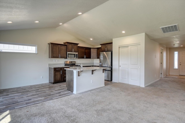 8115 W 57th Ave, Spokane, WA 99224 - kitchen with appliances with stainless steel finishes, a kitchen bar, a kitchen island with sink, dark brown cabinets, and lofted ceiling