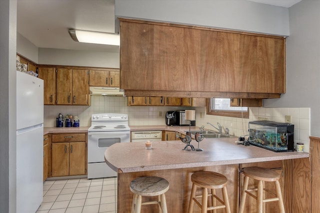 5022 W Garden Springs Ave Unit 5024W, Garden Springs, Spokane, WA 99224 - kitchen with white appliances, under cabinet range hood, brown cabinets, a peninsula, and decorative backsplash