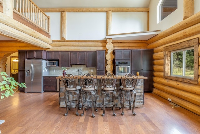 15611 W Pine Bluff Rd, Nine Mile Falls, WA 99026 - kitchen with stainless steel appliances, log walls, a high ceiling, dark brown cabinetry, and a kitchen bar