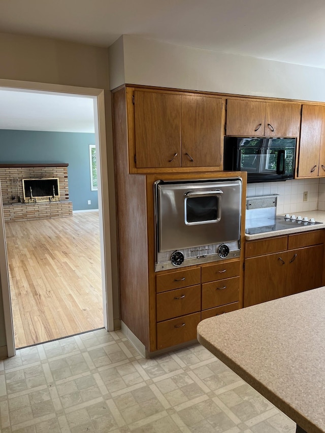 10520 N College Cir, Spokane, WA 99218 - kitchen with black appliances, light flooring, brown cabinets, a fireplace, and tasteful backsplash