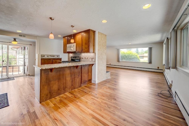 1003 W Eastmont Way, Spokane, WA 99208 - kitchen with white microwave, a baseboard radiator, stainless steel range oven, brown cabinetry, and recessed lighting
