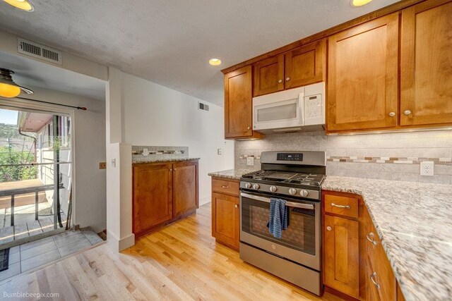 1003 W Eastmont Way, Spokane, WA 99208 - kitchen with white microwave, stainless steel gas range, brown cabinetry, backsplash, and recessed lighting