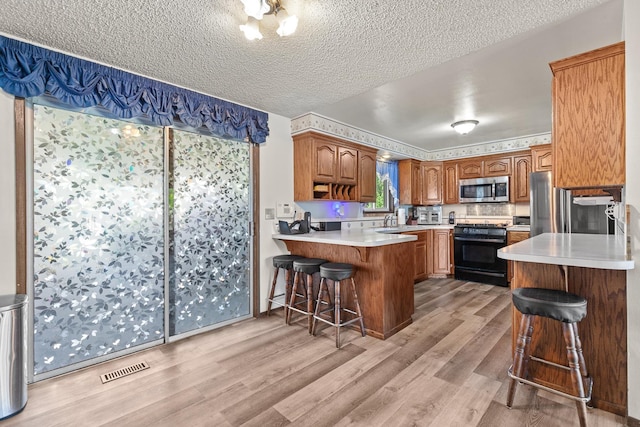 13015 E Mallon Ct, Spokane Valley, WA 99216 - kitchen with stainless steel microwave, black gas stove, a peninsula, light wood finished floors, and a breakfast bar