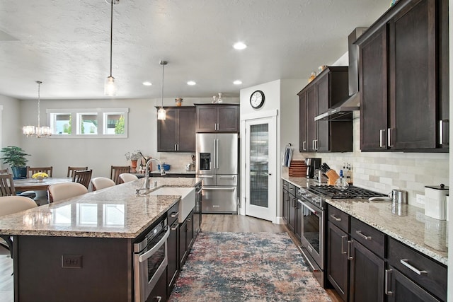 2630 S Fairmont Estates Ct, Greenacres, WA 99016 - kitchen with premium appliances, wall chimney range hood, light wood-style flooring, dark brown cabinetry, and a chandelier