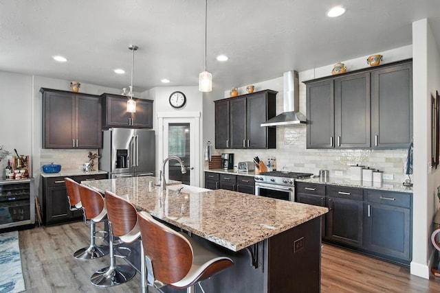 2630 S Fairmont Estates Ct, Greenacres, WA 99016 - kitchen featuring wall chimney range hood, appliances with stainless steel finishes, beverage cooler, light wood-style flooring, and an island with sink