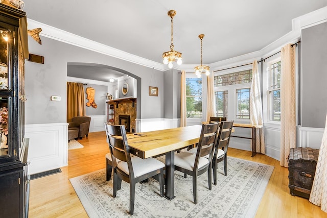 2420 S Cherry Ln, Spokane, WA 99223 - dining space with arched walkways, a fireplace, ornamental molding, a wainscoted wall, and light wood-style floors
