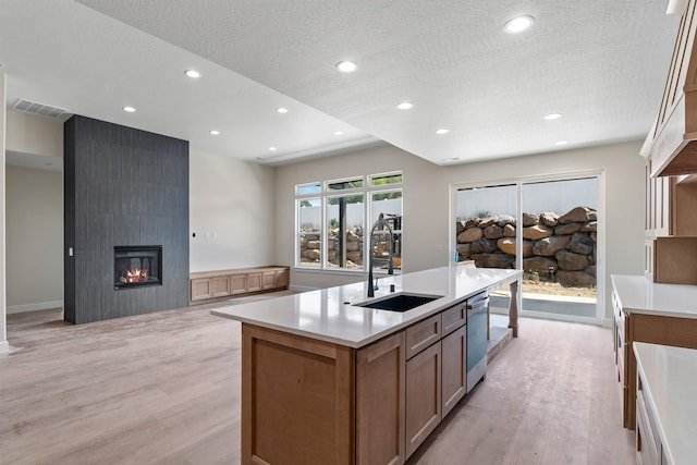 13306 N Starling Ln, Spokane, WA 99208 - kitchen with light wood-type flooring, a large fireplace, an island with sink, a textured ceiling, and light countertops