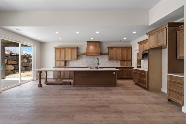 13306 N Starling Ln, Spokane, WA 99208 - kitchen featuring stainless steel microwave, custom range hood, light countertops, a kitchen island with sink, and wood finished floors