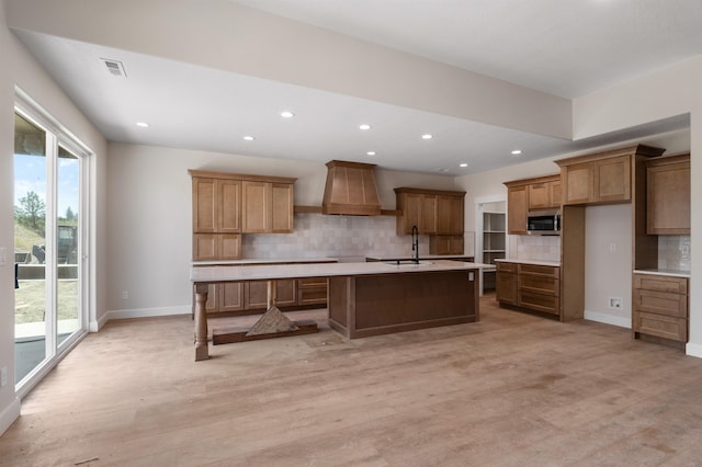 13306 N Starling Ln, Spokane, WA 99208 - kitchen featuring premium range hood, stainless steel microwave, light wood-type flooring, decorative backsplash, and a kitchen island with sink