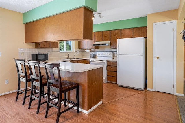 4129 E 32nd Ave, Spokane, WA 99223 - kitchen featuring white appliances, under cabinet range hood, a peninsula, brown cabinetry, and light countertops