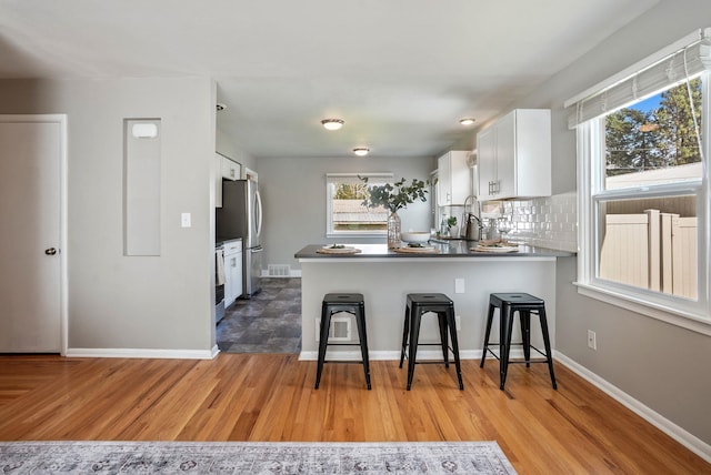 5204 N Maple St, Spokane, WA 99205 - kitchen with freestanding refrigerator, white cabinets, a peninsula, a kitchen breakfast bar, and tasteful backsplash
