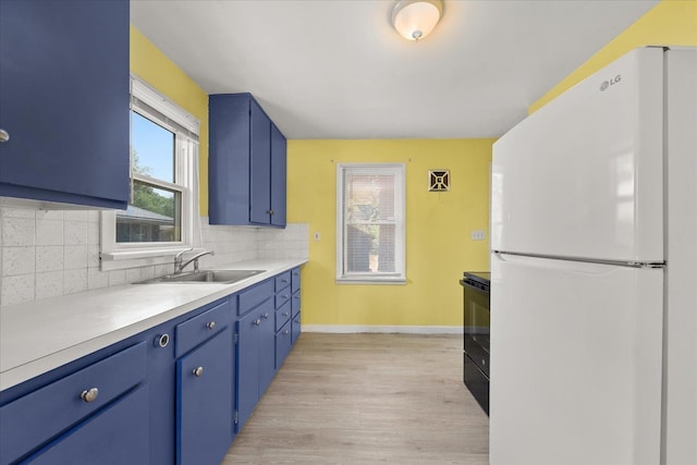 3829 W Broad Ave, Spokane, WA 99205 - kitchen with freestanding refrigerator, blue cabinetry, backsplash, and light wood-style floors