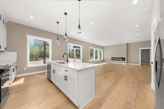 6571 Kate Dr, Nine Mile Falls, WA 99206 - kitchen with stainless steel appliances, light wood-style floors, white cabinetry, a glass covered fireplace, and recessed lighting