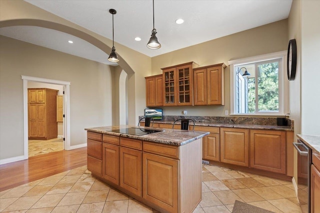 7105 S Saddle Ridge Ln, Spokane Valley, WA 99016 - kitchen with brown cabinets, arched walkways, a kitchen island with sink, pendant lighting, and dark stone countertops