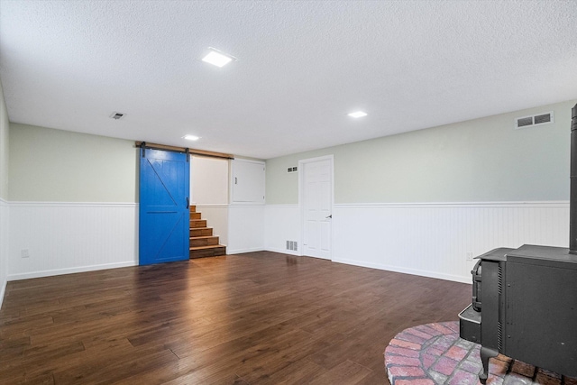 317 E Eaton Ave, Spokane, WA 99218 - unfurnished living room featuring a wood stove, wainscoting, a barn door, dark wood-style floors, and a textured ceiling