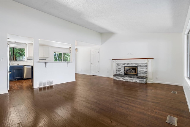 317 E Eaton Ave, Spokane, WA 99218 - unfurnished living room with dark wood-style flooring, a stone fireplace, vaulted ceiling, and a textured ceiling