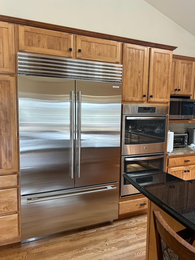 6815 S Palouse Hwy, Spokane, WA 99223 - kitchen with appliances with stainless steel finishes, dark stone countertops, vaulted ceiling, light wood-style flooring, and brown cabinets
