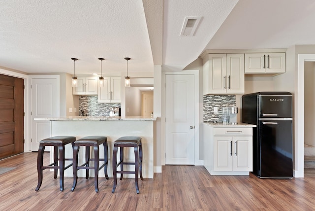 6221 N Highview Ln, Spokane Valley, WA 99217 - kitchen featuring freestanding refrigerator, decorative backsplash, wood finished floors, a kitchen bar, and a textured ceiling