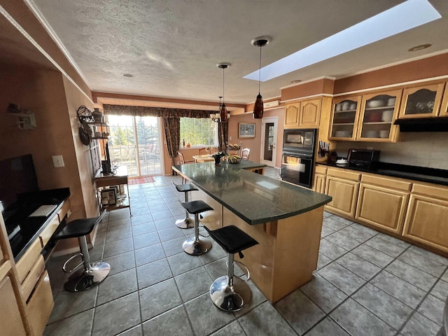 1703 W 25th Ave, Spokane, WA 99224 - kitchen with dark countertops, a kitchen breakfast bar, black microwave, glass insert cabinets, and light brown cabinets