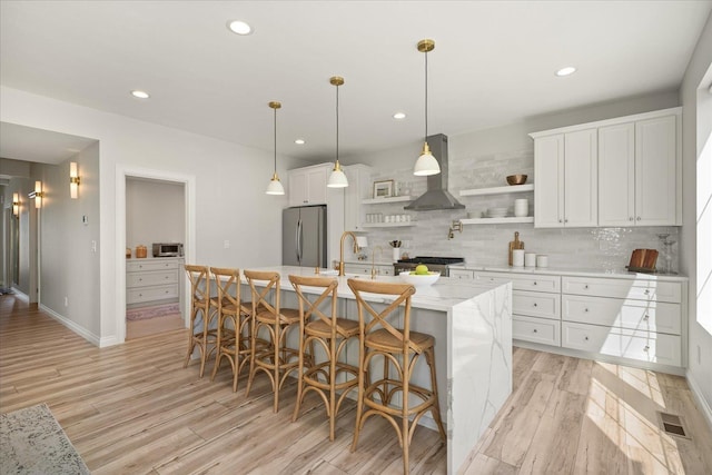 4620 E 43rd Ave, Spokane, WA 99223 - kitchen with freestanding refrigerator, wall chimney range hood, light wood-style flooring, tasteful backsplash, and white cabinets