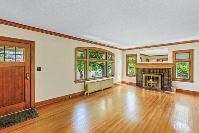 1107 W 19th Ave, Spokane, WA 99203 - unfurnished living room with radiator heating unit, light wood-style flooring, ornamental molding, a brick fireplace, and a textured ceiling