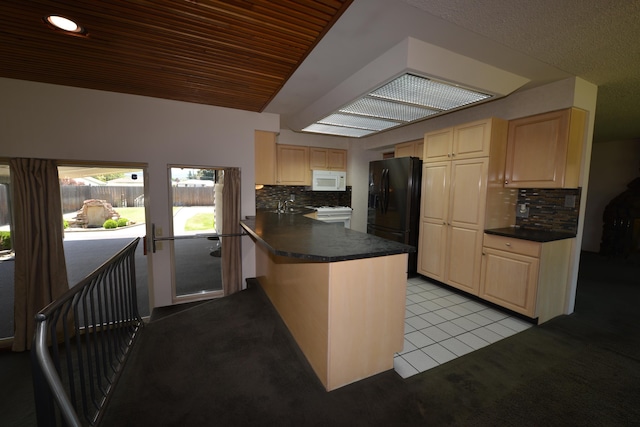 7516 E Baldwin Ave, Spokane Valley, WA 99212 - kitchen with black fridge, white microwave, a peninsula, dark countertops, and backsplash
