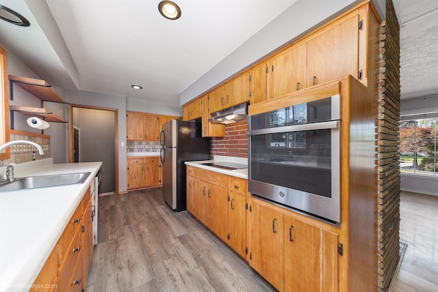 11918 E Grace Ave, Spokane Valley, WA 99206 - kitchen with appliances with stainless steel finishes, under cabinet range hood, decorative backsplash, light countertops, and light wood-style flooring
