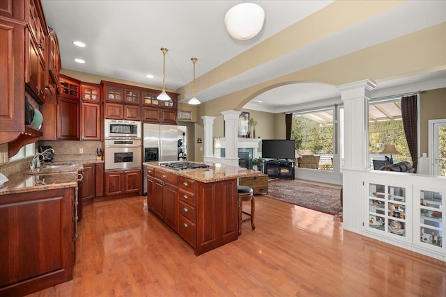 2008 S Zephyr Rd, Liberty Lake, WA 99019 - kitchen with appliances with stainless steel finishes, decorative columns, arched walkways, a breakfast bar, and light wood-type flooring
