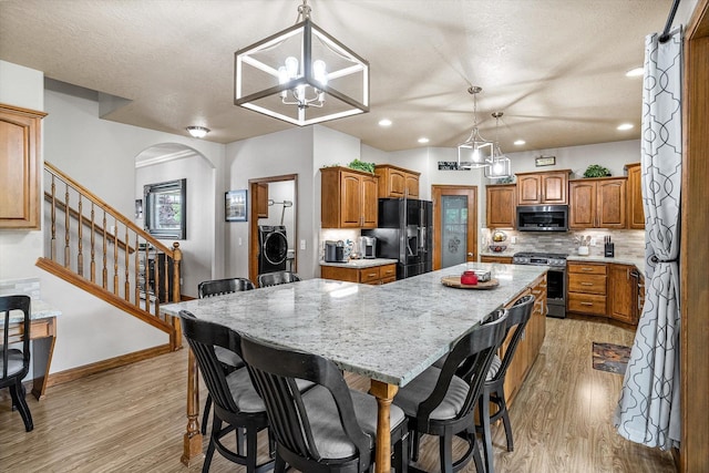 2813 S Steen Ln, Greenacres, WA 99016 - kitchen with stainless steel appliances, a kitchen island, light wood-style floors, washer / clothes dryer, and backsplash