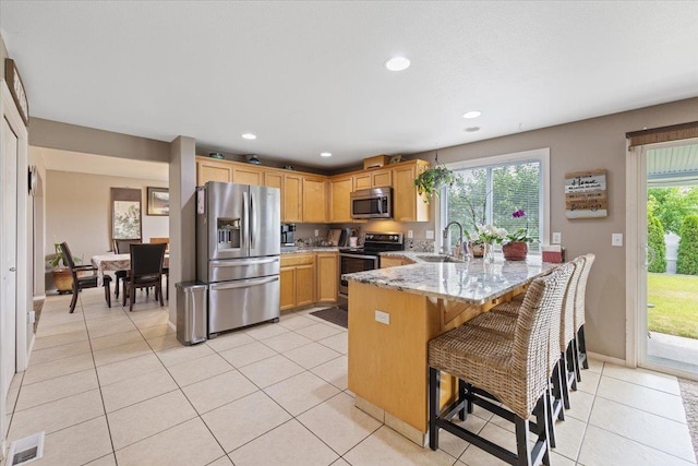 9713 W Sage Ct, Cheney, WA 99004 - kitchen featuring appliances with stainless steel finishes, a peninsula, light stone counters, light tile patterned floors, and a kitchen bar