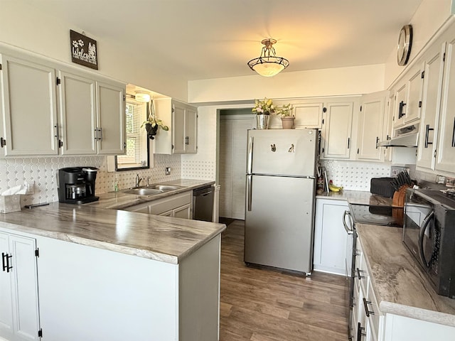 1710 E Crown Ave, Spokane, WA 99207 - kitchen with appliances with stainless steel finishes, a peninsula, under cabinet range hood, decorative backsplash, and wood finished floors